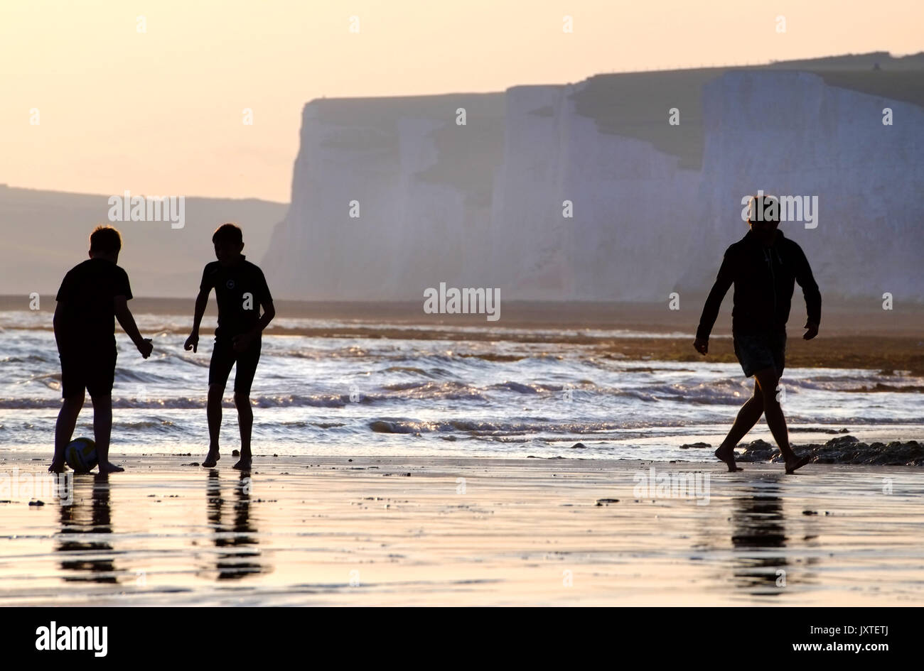 Father and sons playing ball games on a beach at sunset, Seven Sisters, South Downs National Park, East Sussex Stock Photo