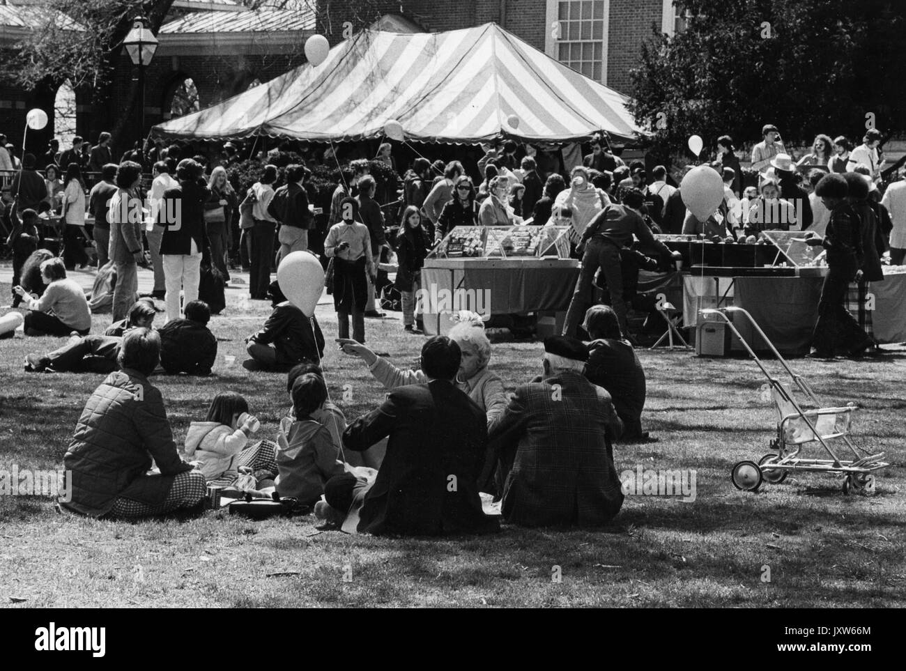 Students sitting in a group at Spring Fair, a Spring carnival, outdoors, vendor tents and a large crowd in the background, at Johns Hopkins University, 1972. Stock Photo