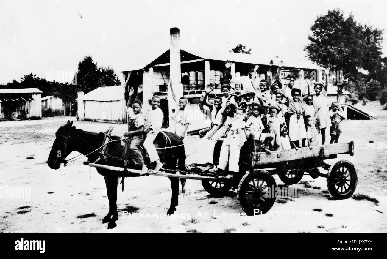 A large group of young African American boys and girls, with smiling and neutral expressions, most of whom have one arm outstretched as if waving, accompanied by a mature African American man and woman, crowded on an open wagon carried by a small horse, which two young boys ride, with the caption 'Pickaninnies at Lewis Plantation' in Brooksville, Florida, 1940. Stock Photo