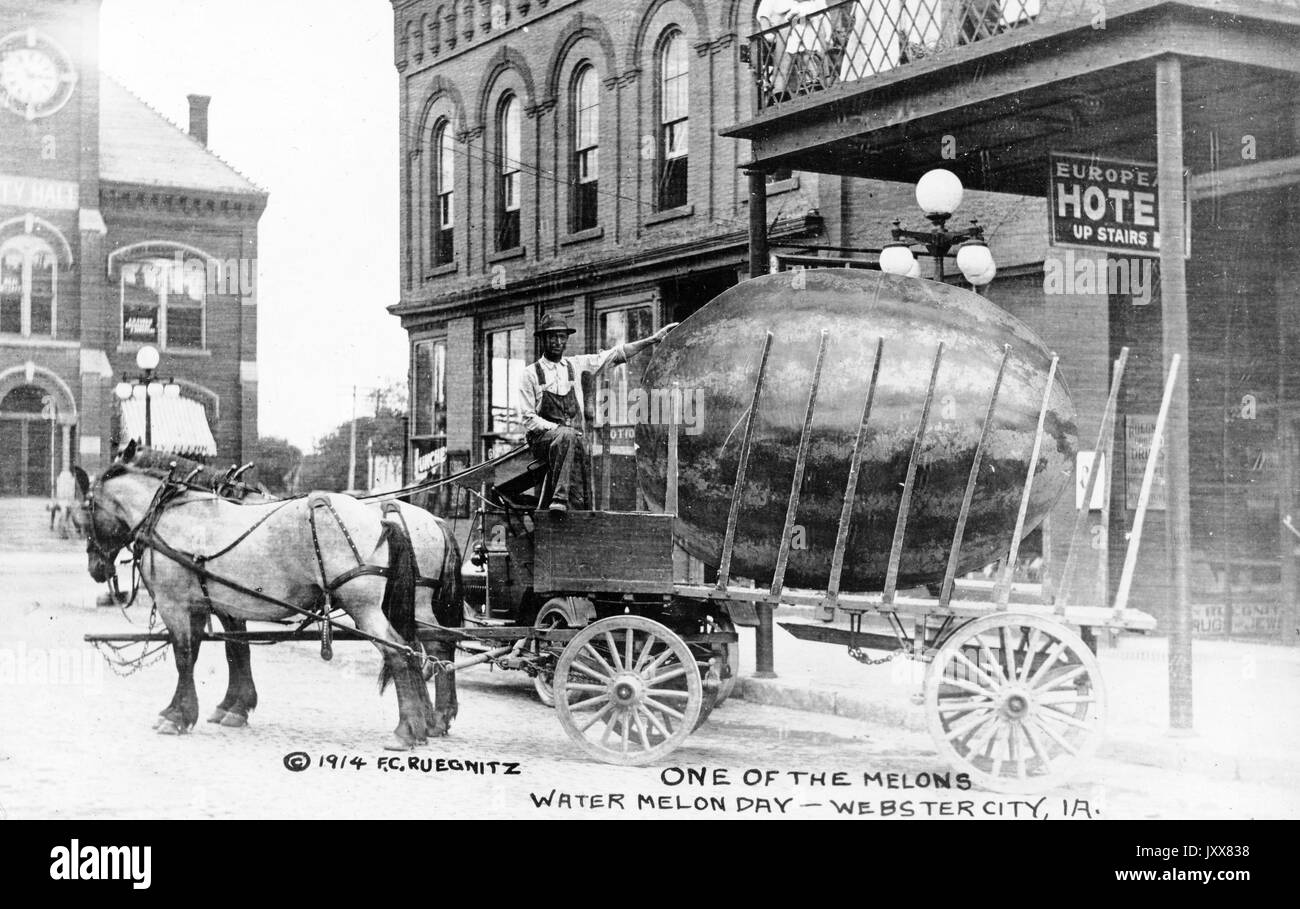 A racially prejudiced depiction of an African American man, who drives an open horse-carried wagon, placing his hand on an over-sized watermelon, which lies in the bed of the wagon on a street in front of a hotel in an American town, with the caption 'One of the melons, Watermelon Day, Webster City, [Iowa]', Europe, 1914. Stock Photo