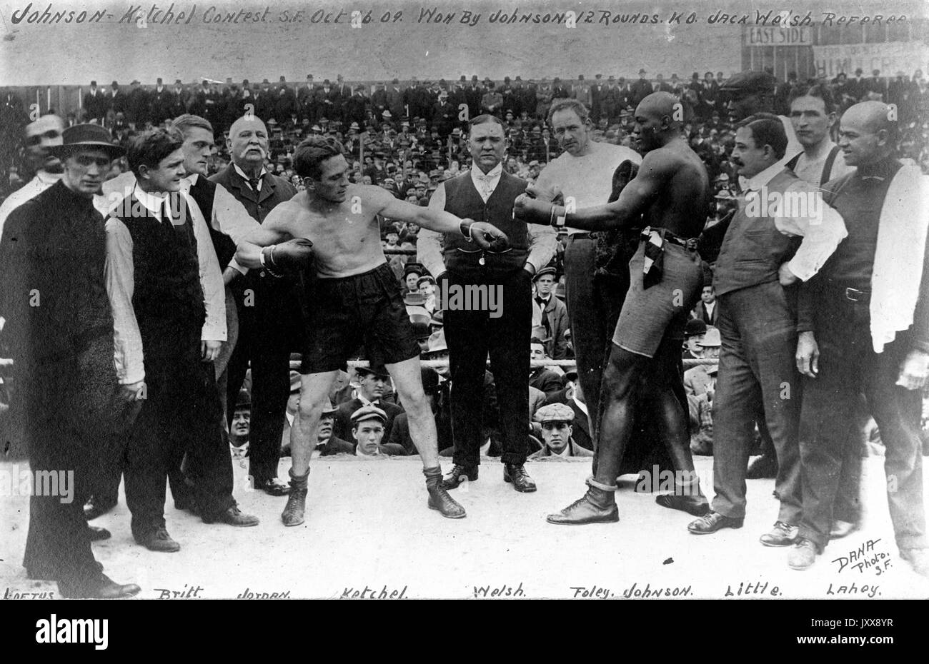 Boxers Stanley Ketchel (center left) and Jack Johnson (center right) stand in the ring before their famous match, with California boxing referee Jack Welsh (center) standing between the two boxers, surrounded by other industry members, in Colma, California, 1909. Stock Photo