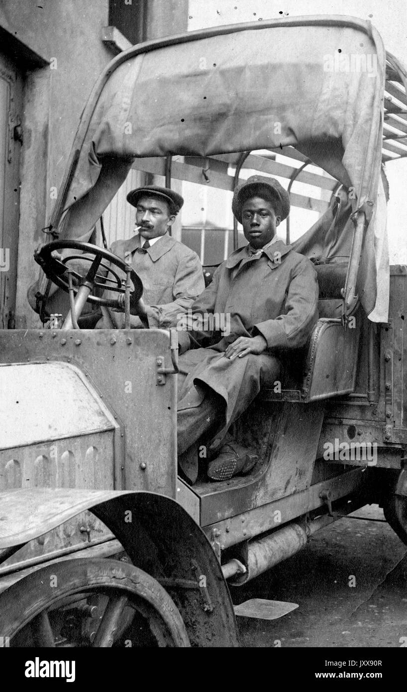 Full length sitting portrait of a mature African American man, who is smoking, and a mature African American woman, both with neutral expressions, in a car, or possibly piece of machinery, 1915. Stock Photo