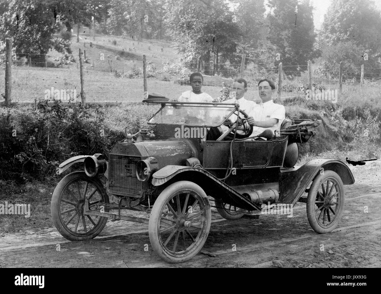 Full length portrait of two men driving a car outdoors, one African American child in the car, 1920. Stock Photo
