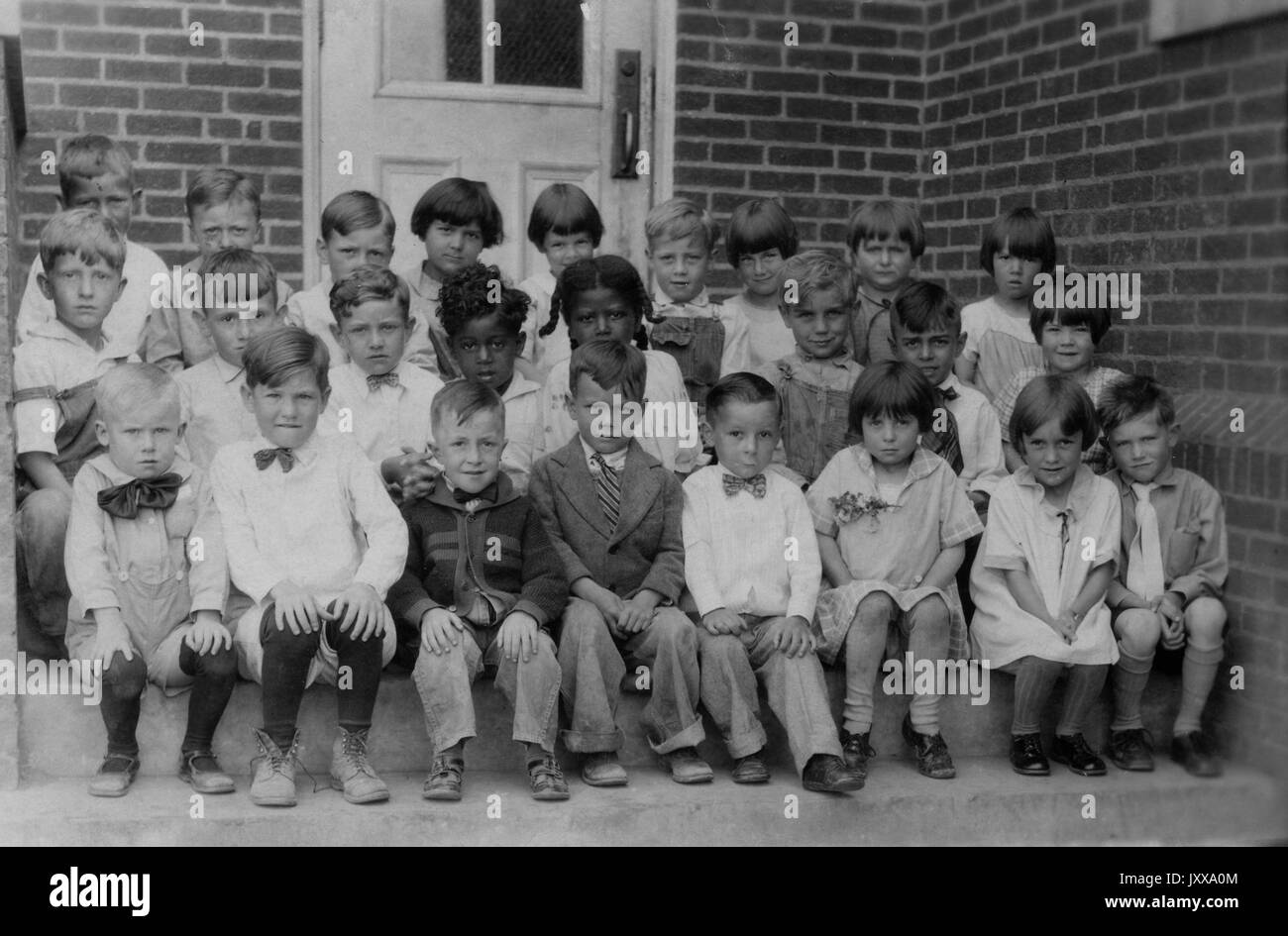 Full length landscape shot of schoolchildren seated on steps in front of building, two African American girls in the middle of the second row, 1927. Stock Photo