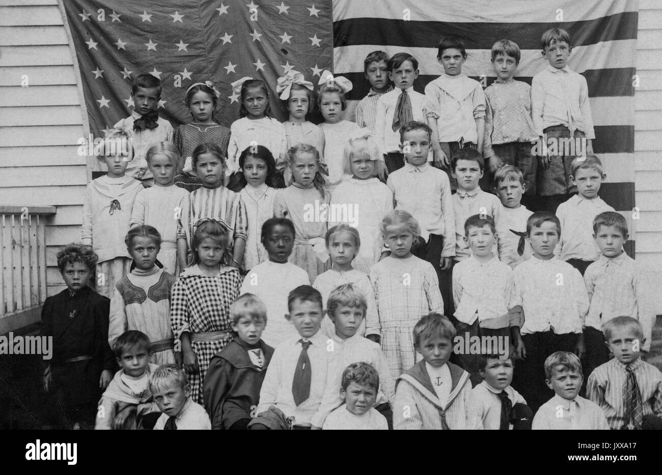 Full length landscape shot of schoolchildren in front of an American flag, one African American girl in the second row, 1920. Stock Photo