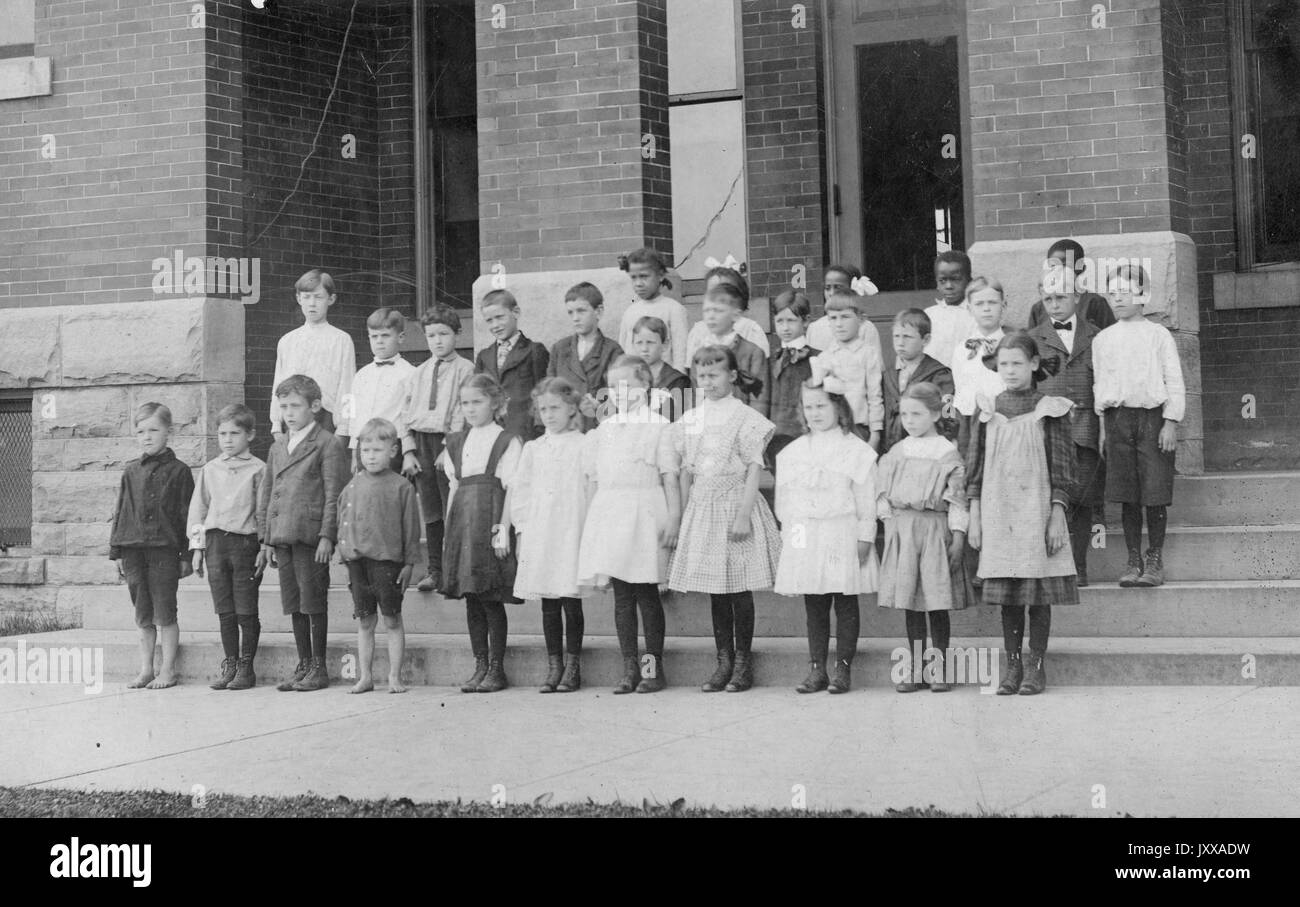 Full length landscape shot of schoolchildren, diagonal shot, all wearing uniforms, standing, one African American student standing in the back, 1920. Stock Photo