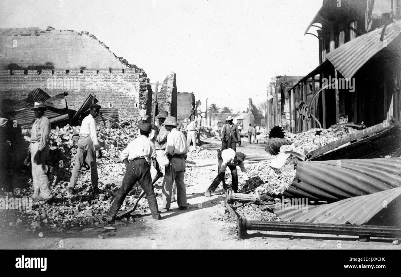 Landscape of African American men rummaging around dilapidated brick buildings, some men leaning down to pick up the shambles of the structures, others inspecting the fallen buildings around them, 1920. Stock Photo