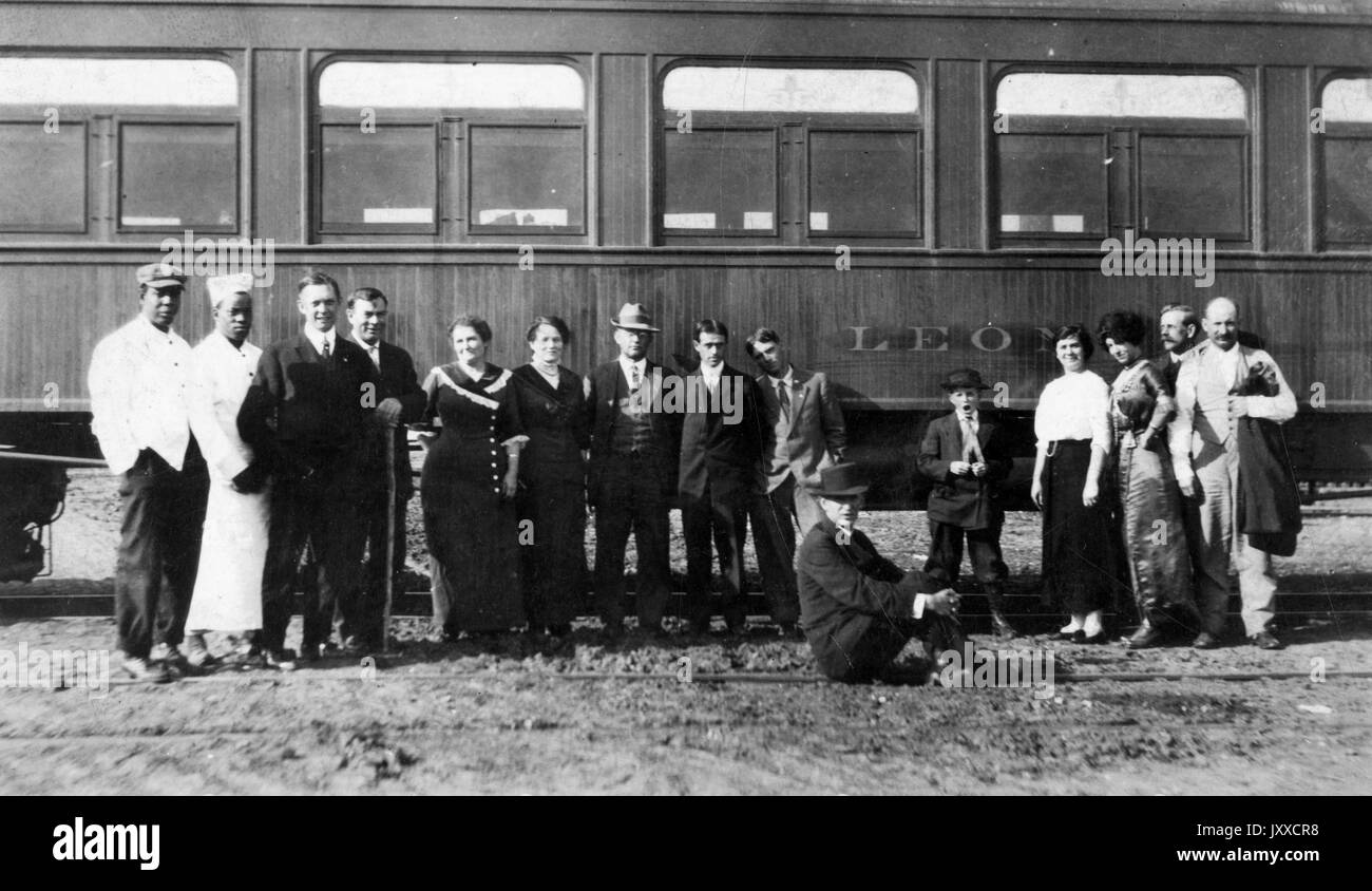 Portrait of fifteen men and women, all standing except one man sitting on the dirt, in front of a train that reads 'Leon, ' some African American, some white, 1925. Stock Photo