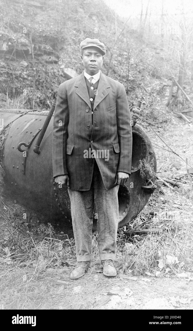 Full length portrait of an African American military officer dressed in uniform, outdoors with some war machinery behind him, neutral facial expression, 1917. Stock Photo