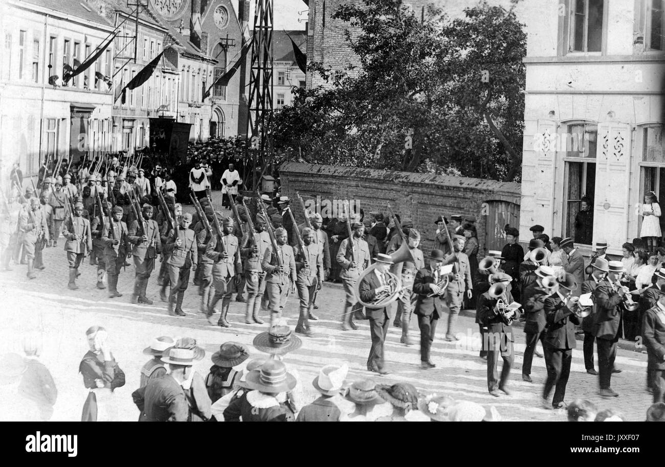 Military parade with military men marching down a street, each carrying a firearm, many viewers look on, 1920. Stock Photo