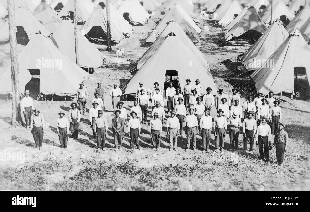 African American soldiers are standing in an organized fashion in front rows of their sleeping tents, they are all wearing hats, dark colored pants and light colored shirts, 1917. Stock Photo