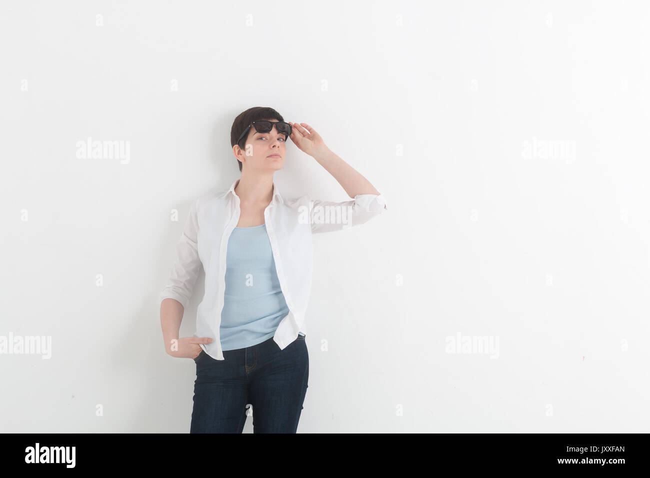 Portrait of young girl in a white shirt and denim jeans with sunglasses on a white background. Stock Photo