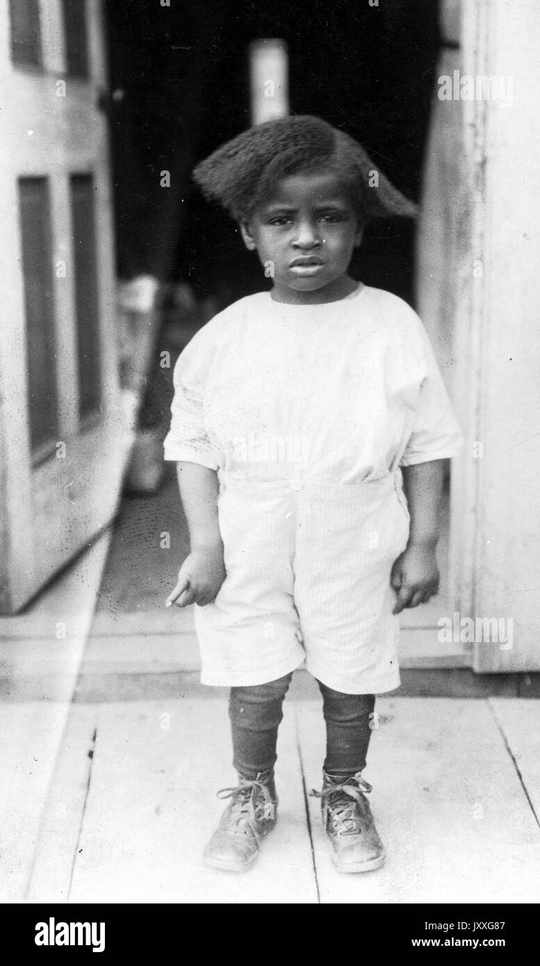 Full length portrait of an African American child, wearing white outfit, shoes, neutral facial expression, 1915. Stock Photo