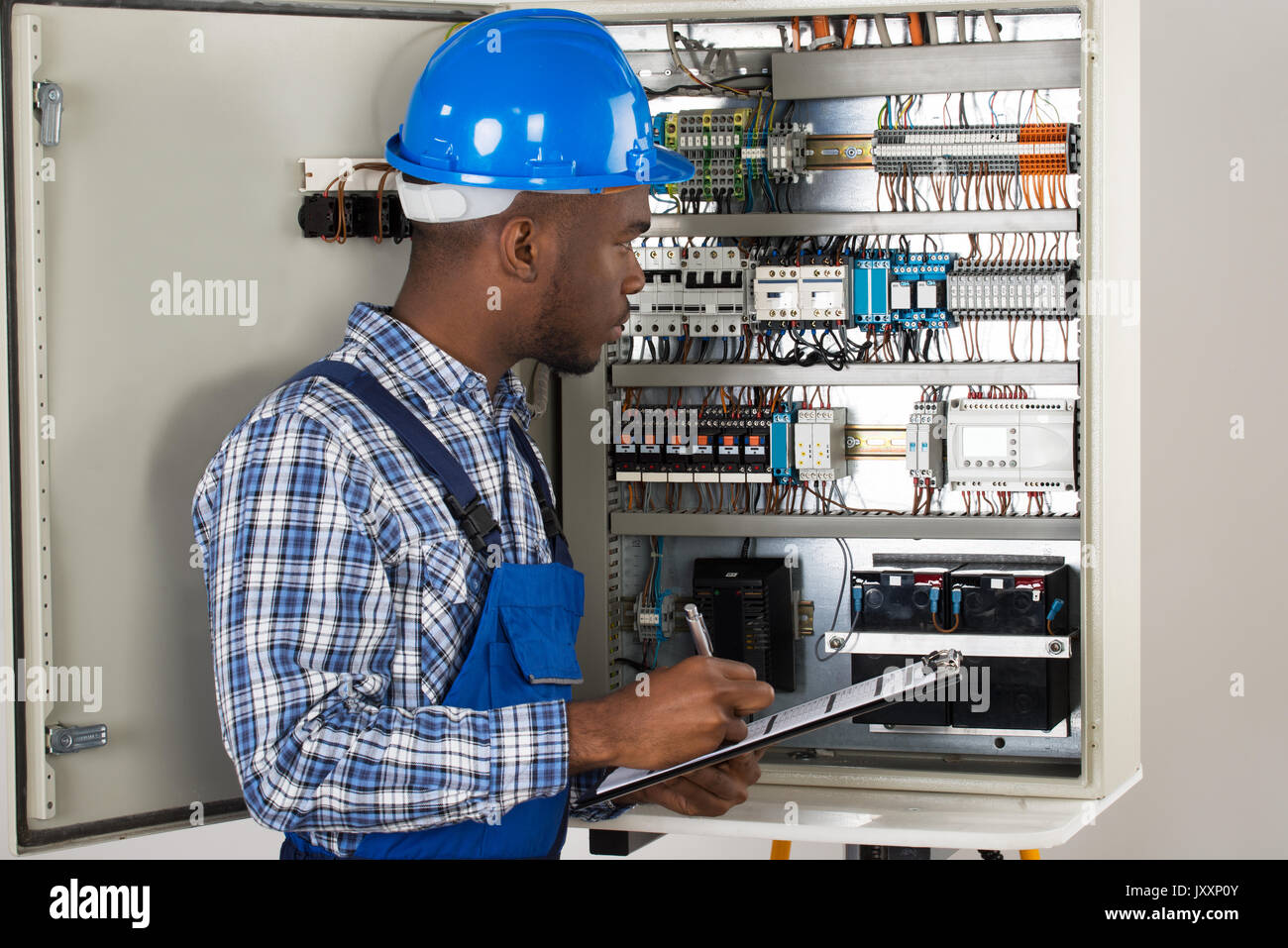 Male Technician Holding Clipboard While Examining Fusebox Stock Photo