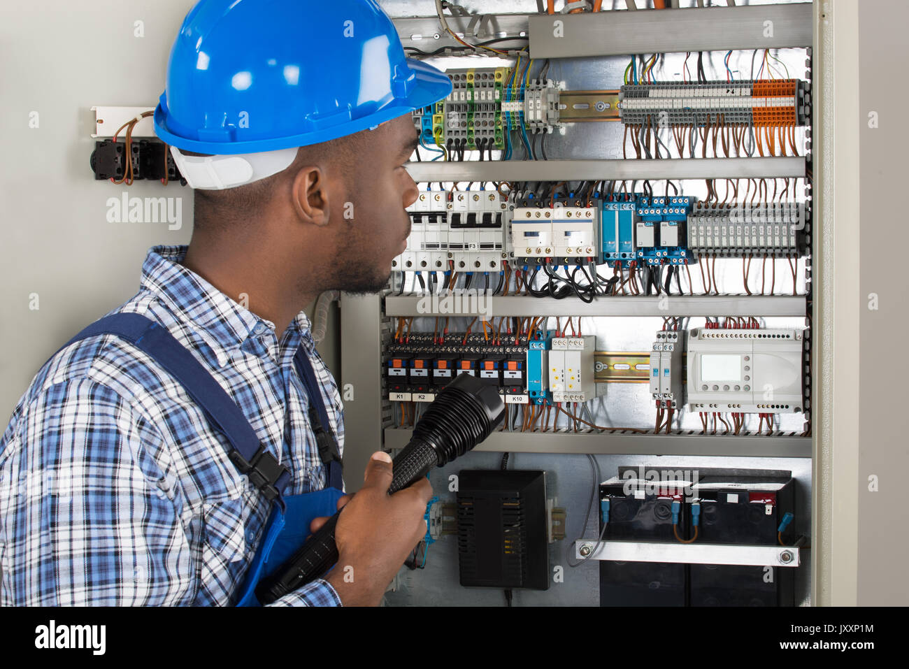 Young African Male Technician Analyzing Fusebox With Flashlight Stock Photo