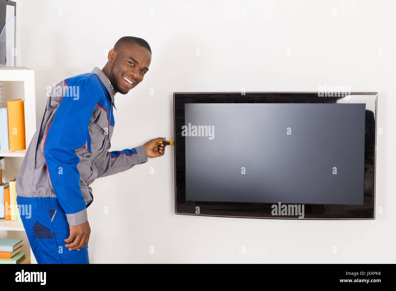 Male African Technician Repairing Television Mounted On Wall Stock