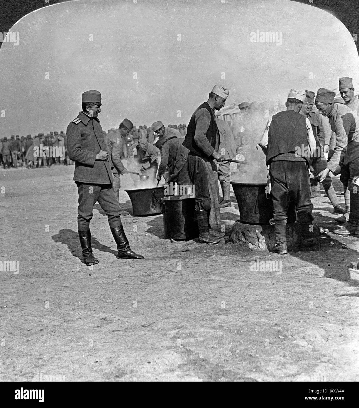 Hungrige Soldaten sammeln sich an dampfenden Kesseln einer Feldküche an der serbischen Front, 1910er Jahre. Hungry soldiers beside steaming caldrons in a field kitchen on the Serbian front, 1910s. Stock Photo