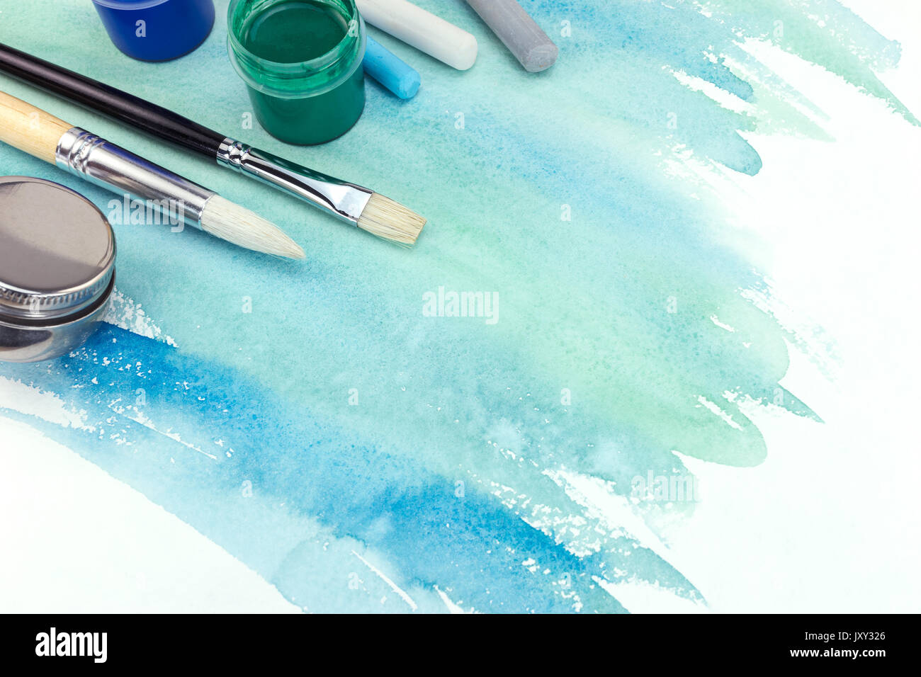 various paintbrushes, paints and pastel chalks on green blue watercolor background Stock Photo