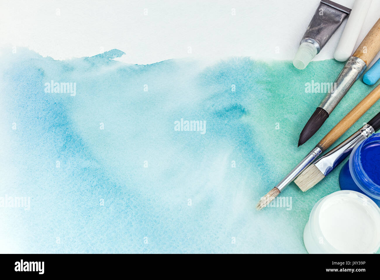 artist paintbrushes and paints over abstract hand painted watercolor background on textured paper Stock Photo