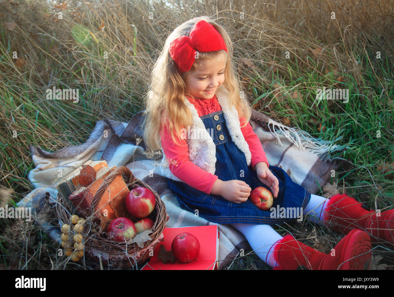 Little girl on nature with a basket of fruit and books. Stock Photo