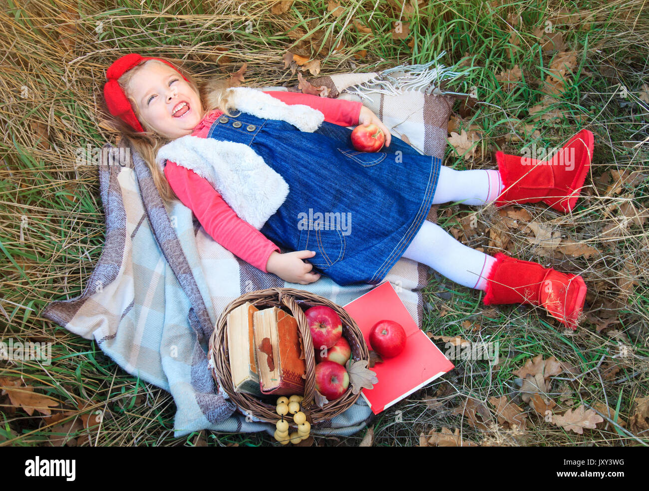Little girl lying in grass on a plaid with a basket of fruit in the autumn day. Stock Photo