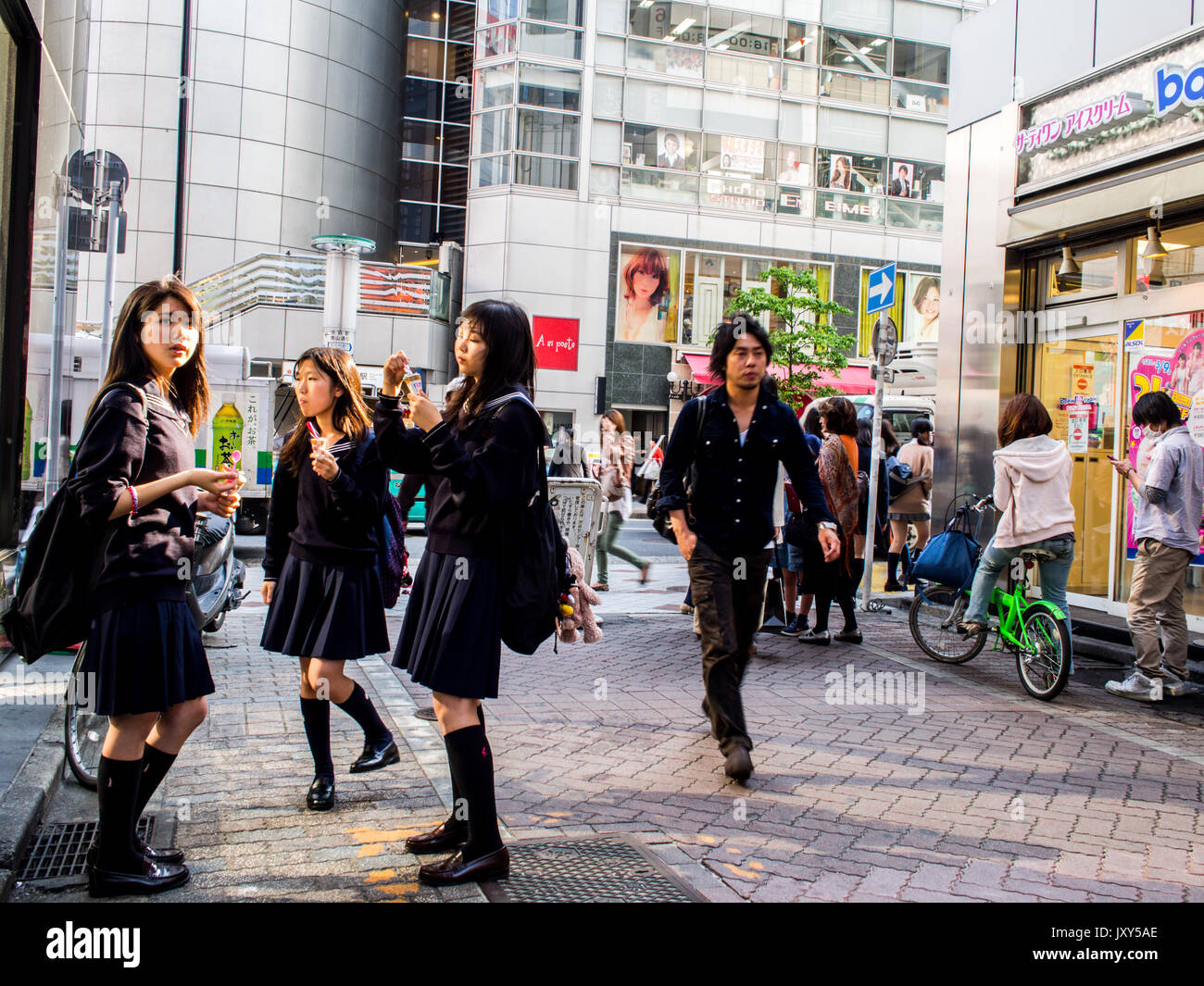 Three schoolgirls in uniform eating ice cream, a man walking past, city street, Shibuya, Tokyo, Japan Stock Photo