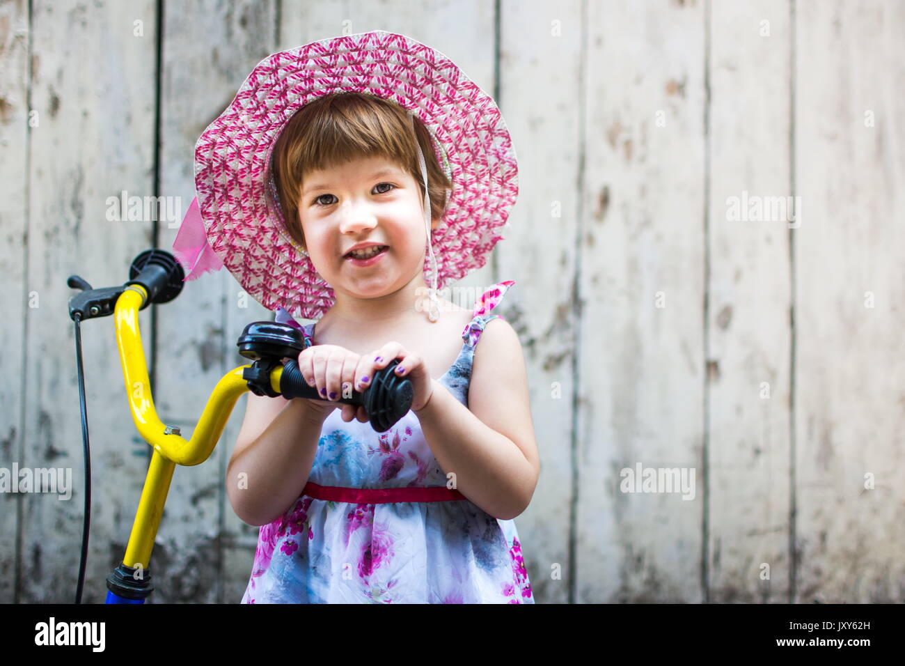 Cute girl with bicycle against vintage wooden backdrop Stock Photo