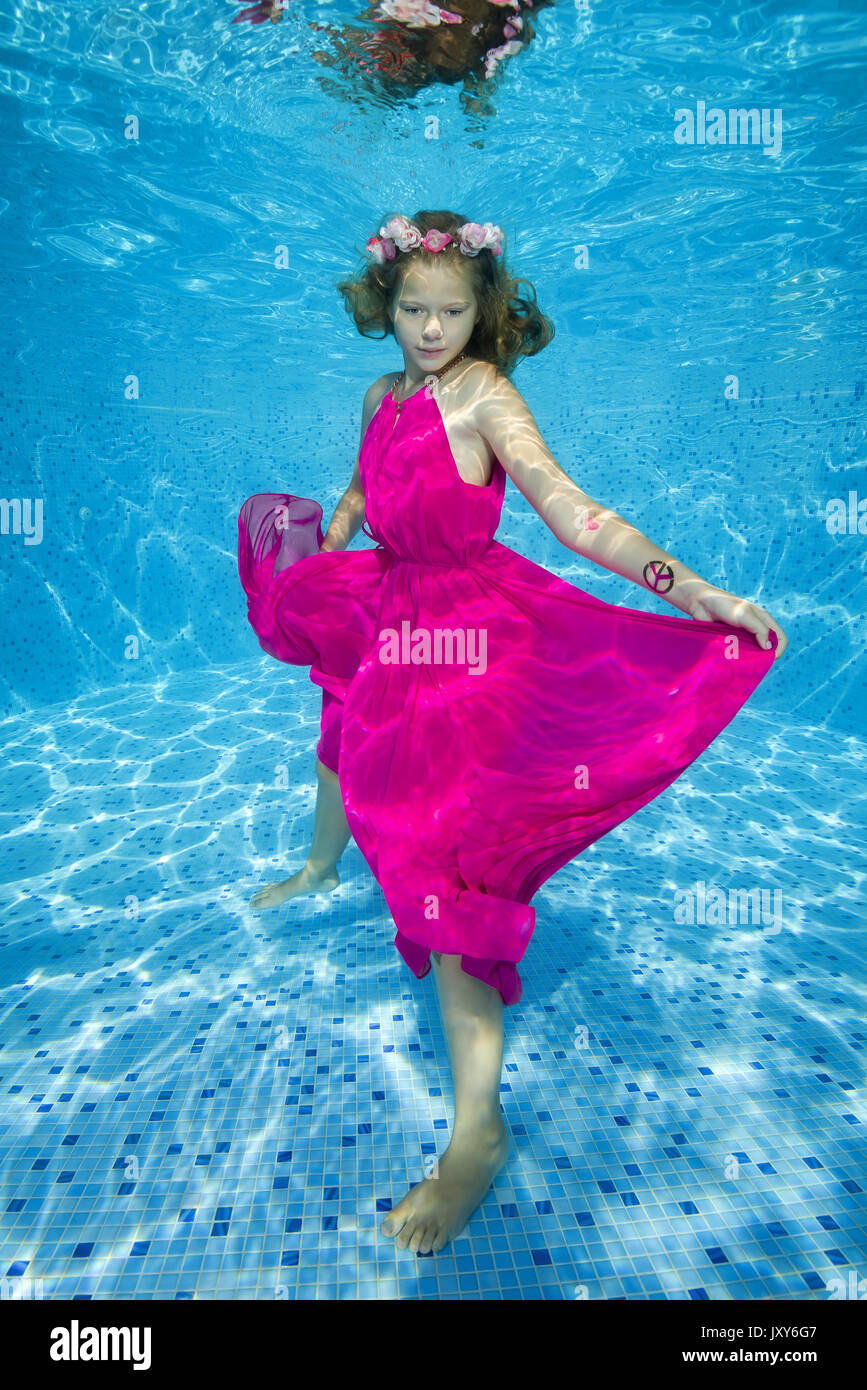A teenage girl in a pink dress posing under the water in a pool Stock Photo