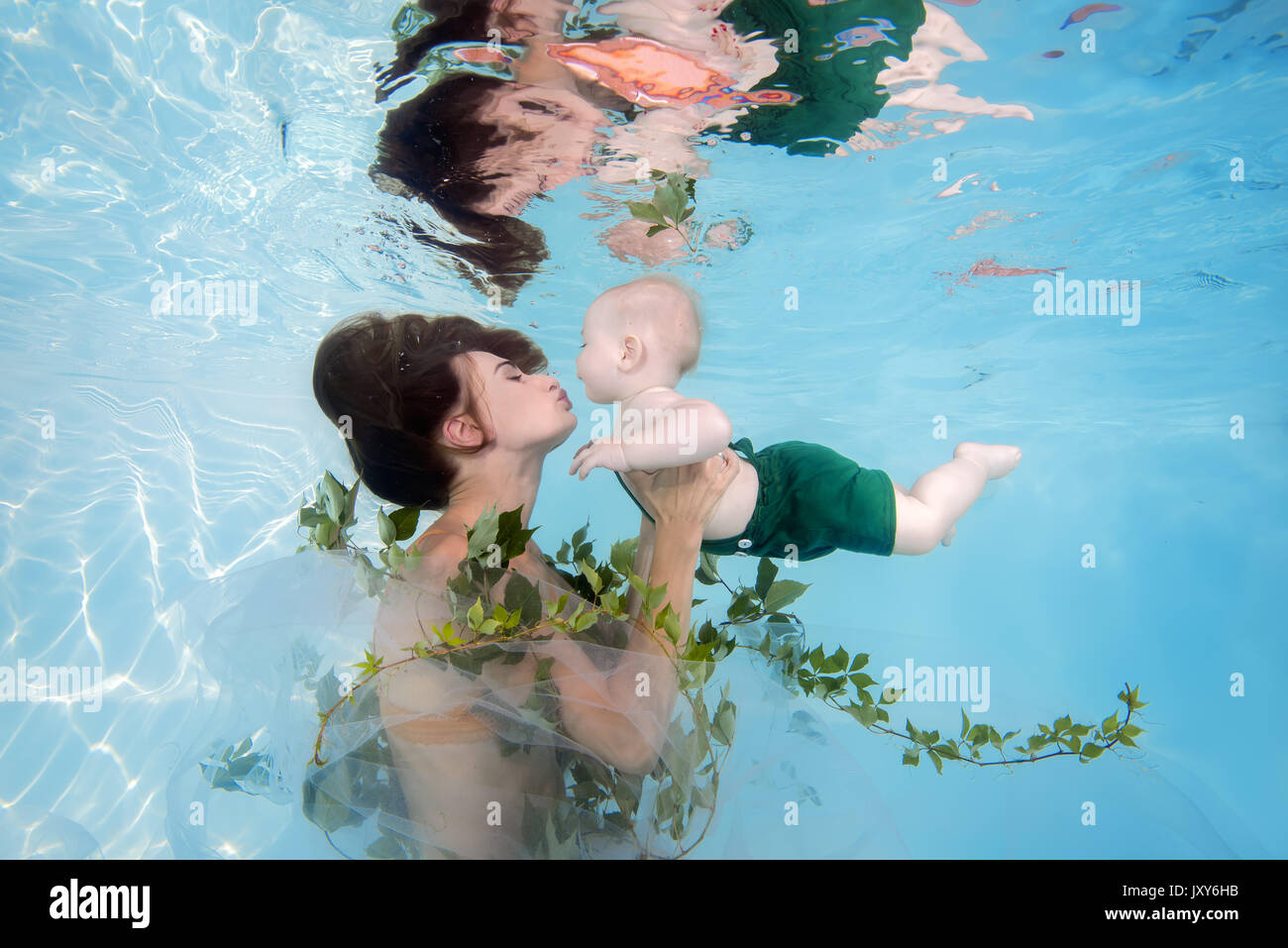 Woman in green dress with little boy posing under water in pool Stock Photo