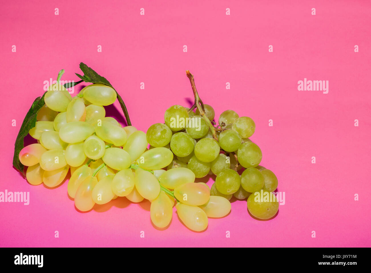 Real and fake white grapes on pink background Stock Photo