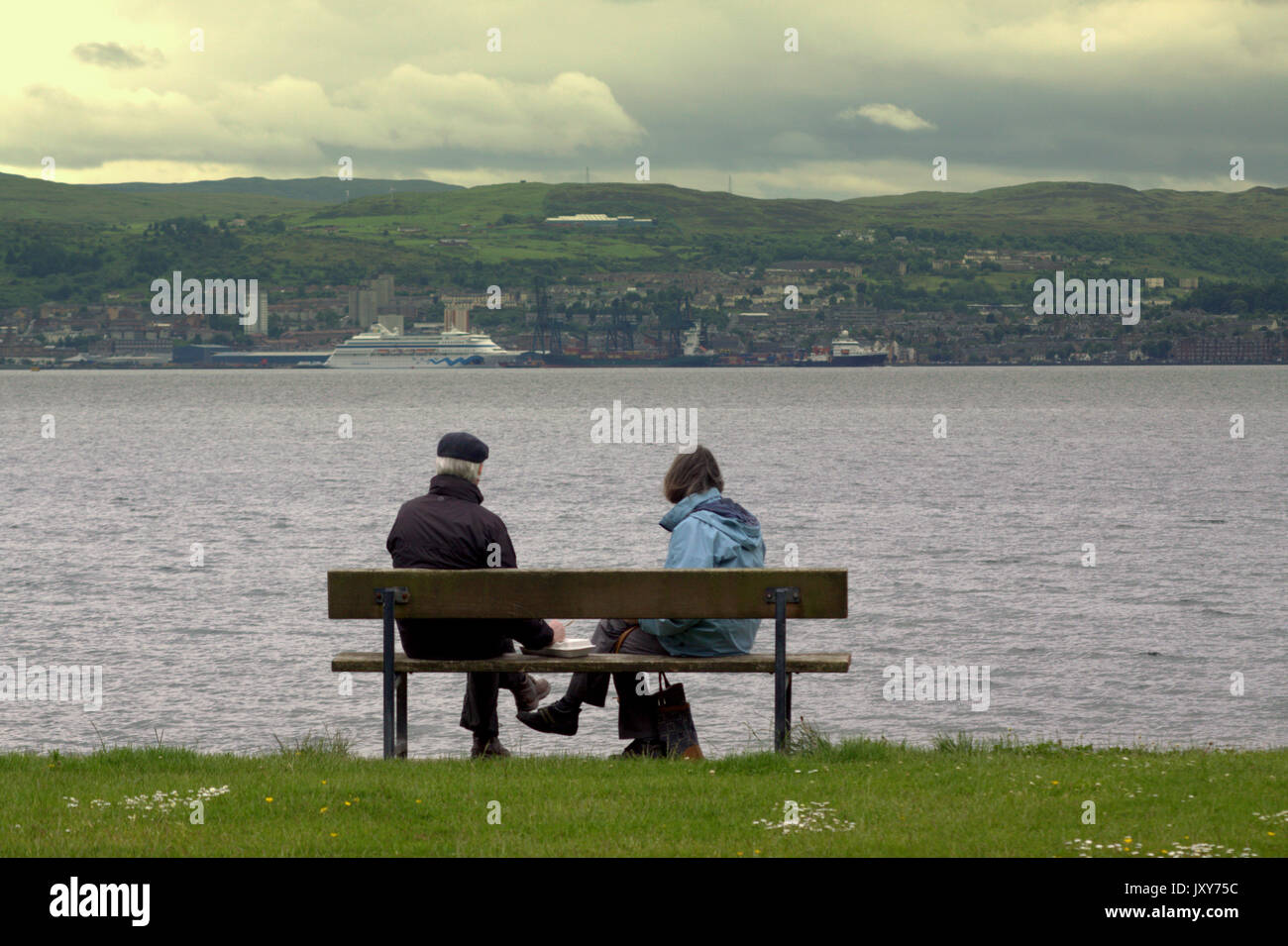 Helensburgh town boardwalk or seafront couple sitting on a bench looking across to Greemock ferry terminal Stock Photo