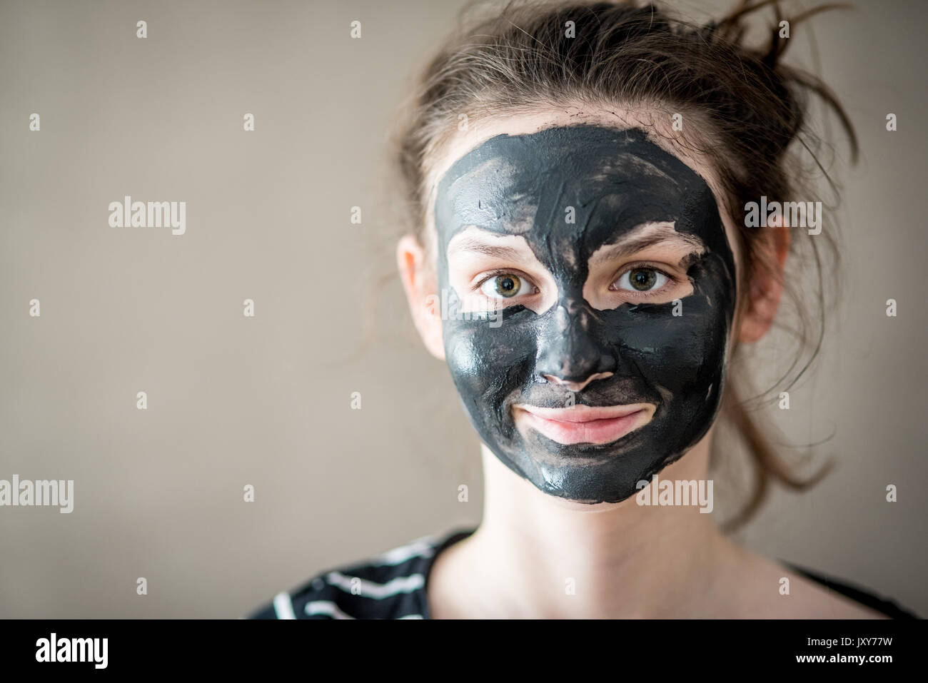 Smiling teenage girl with black cosmetic mask on her face Stock Photo