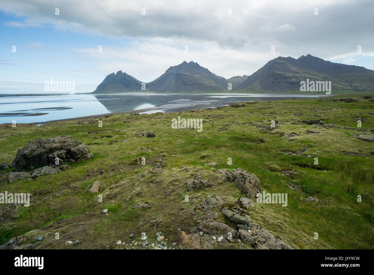 Iceland - Three mountains reflecting in silent water of lake behind green landscape Stock Photo