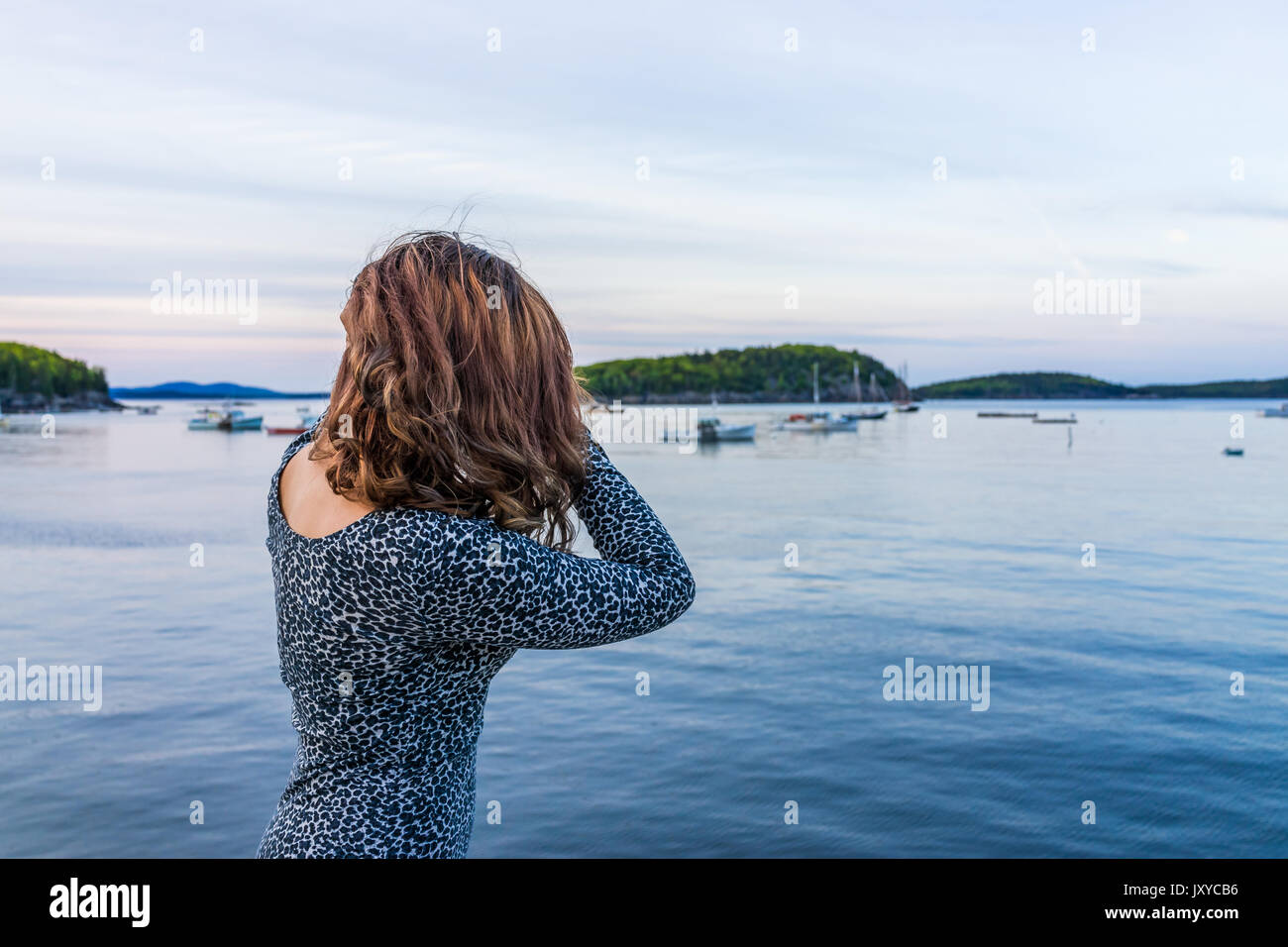 Portrait of back of young woman touching hair on edge of dock in Bar Harbor, Maine at sunset Stock Photo