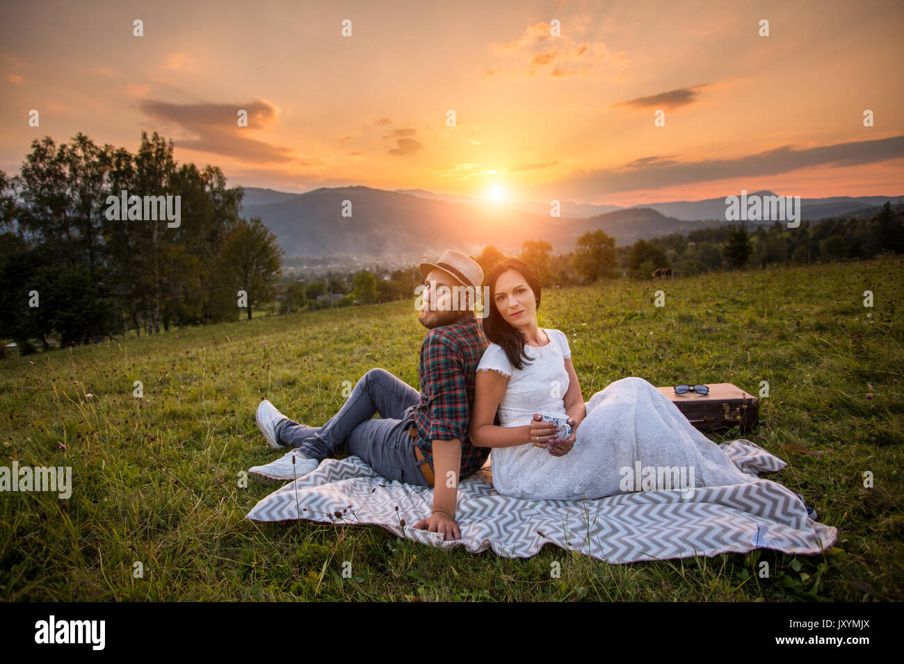 couple in love on a white plaid in a field on a picnic. against a background of a sunset in the mountains. romance. hdr photo Stock Photo