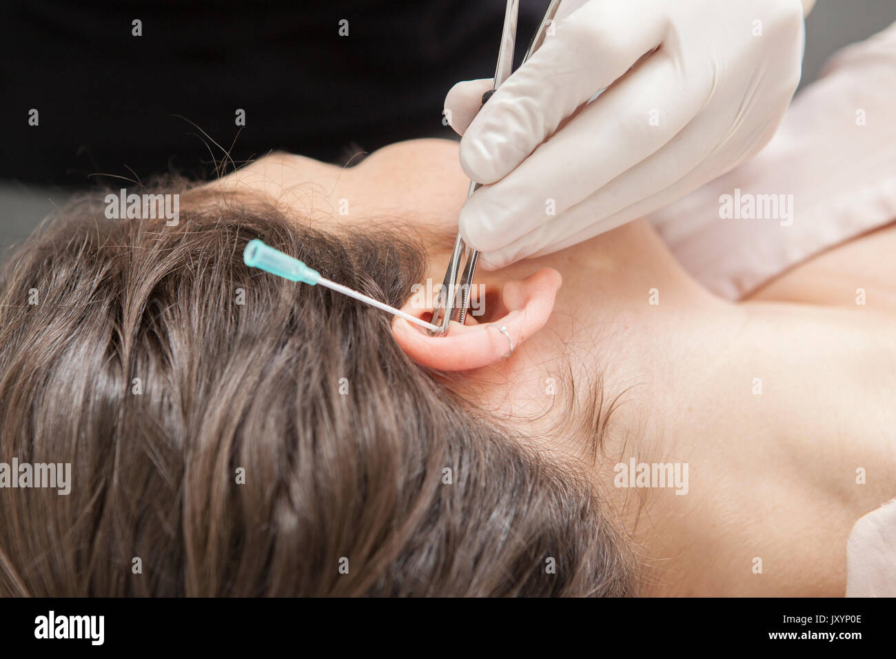 Professional making a piercing hole on ear with indwelling cannula method. Rook type. Holding the cannula Stock Photo