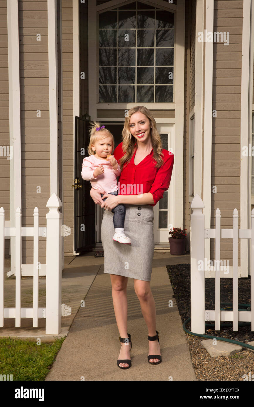 Caucasian mother posing near house with baby daughter Stock Photo