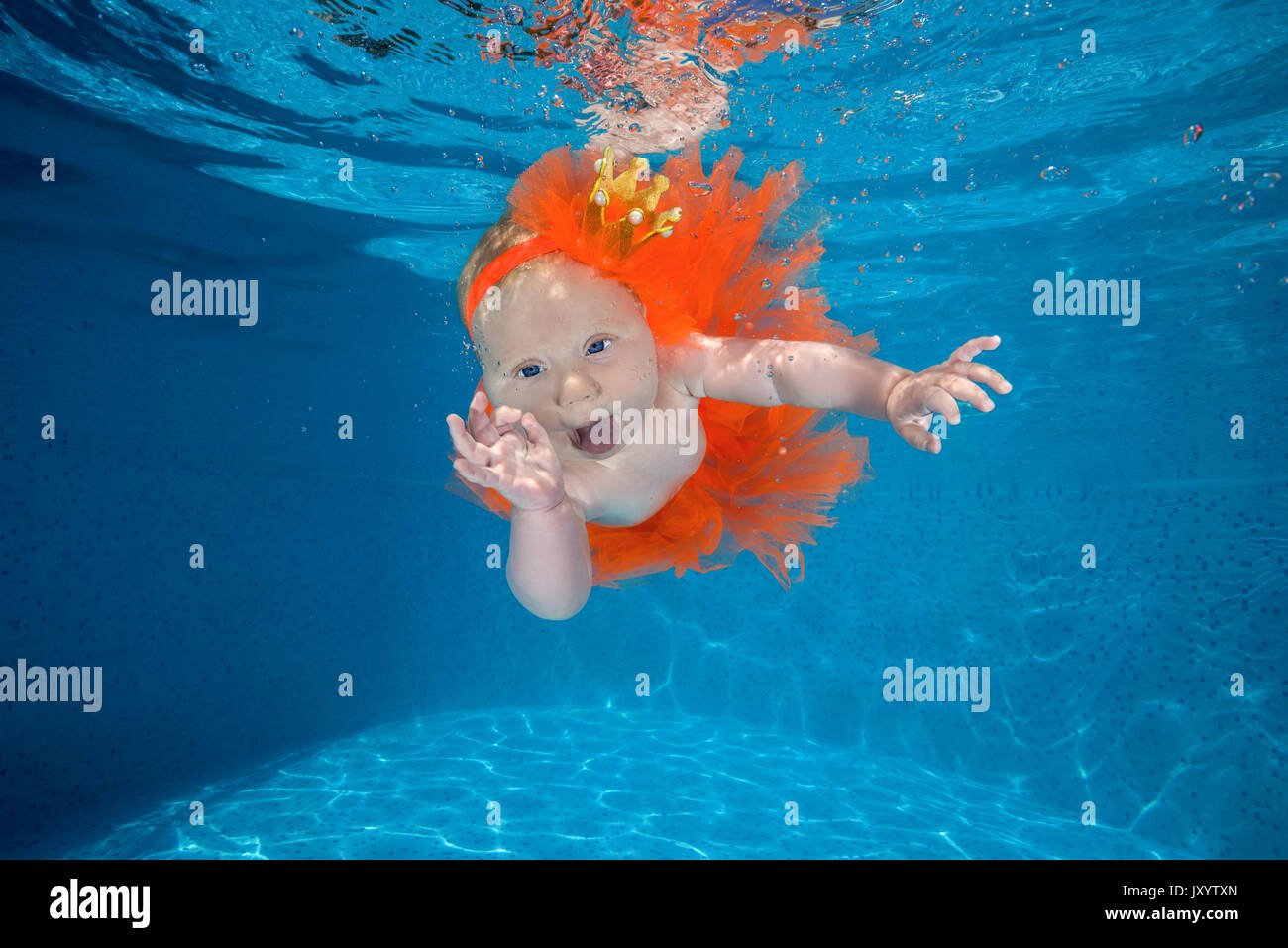 A little girl dressed as a princess under water in a pool. AMUSING shots show the exhilarated and confused faces water babies can pull when dunked int Stock Photo