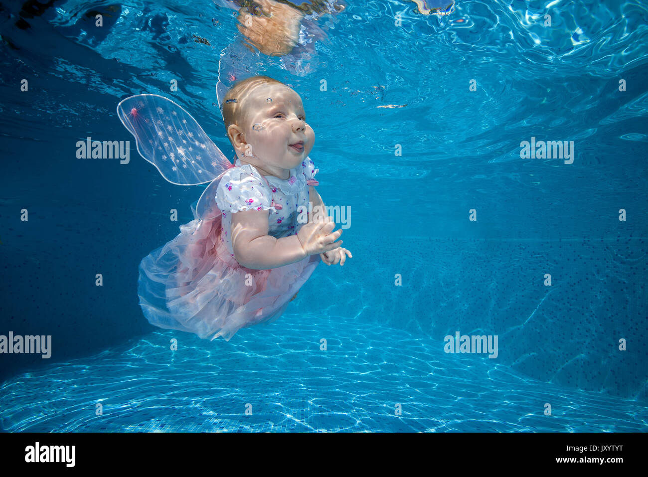 Little girl in fairy dress under water in the pool. AMUSING shots show the exhilarated and confused faces water babies can pull when dunked into swimm Stock Photo