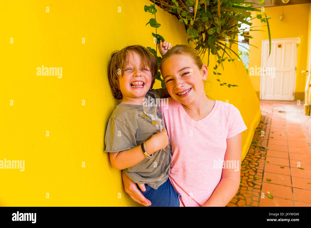 Caucasian girl leaning on yellow wall holding brother Stock Photo