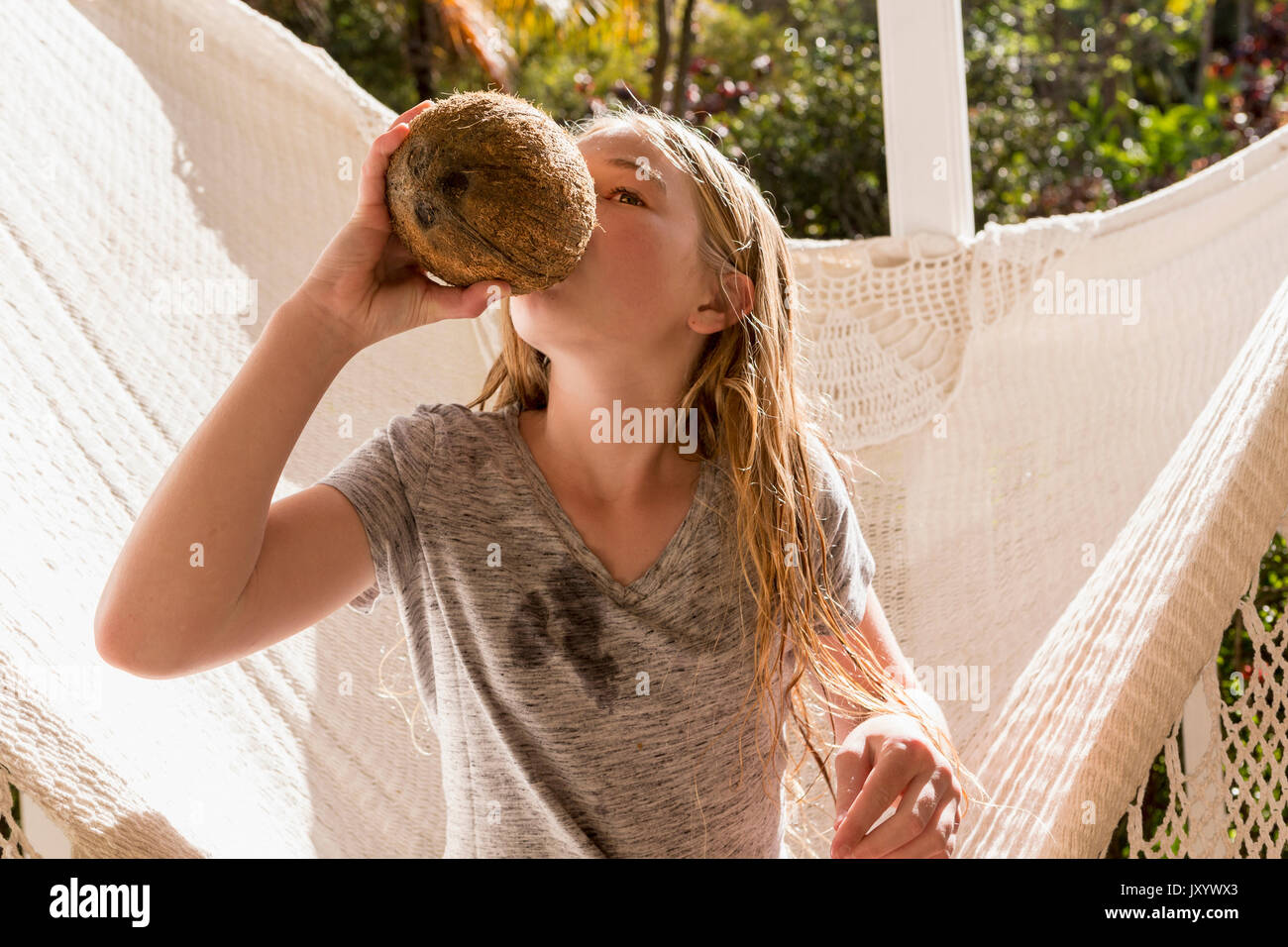 Caucasian girl sitting in hammock drinking from coconut Stock Photo