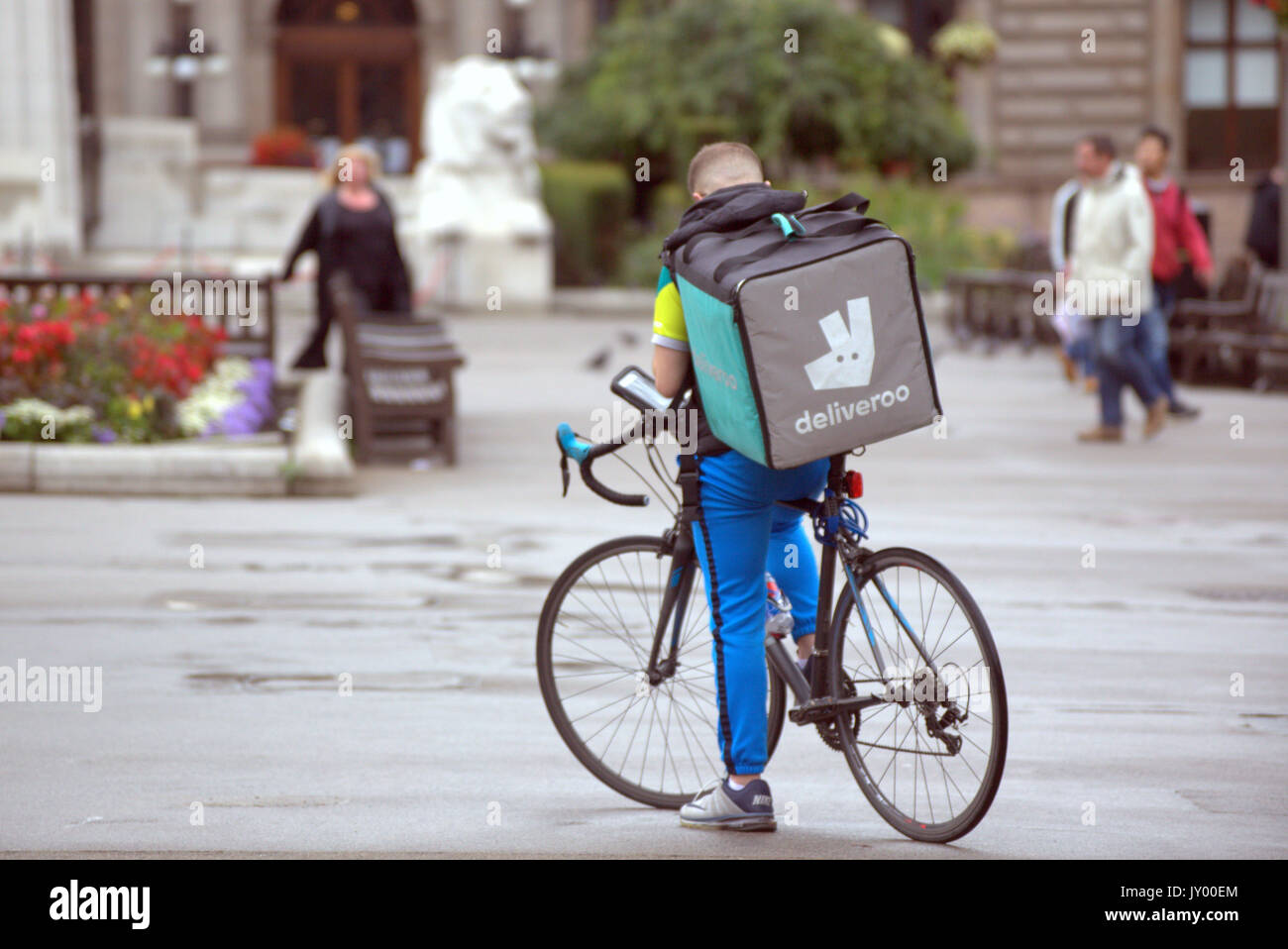 wet George square Glasgow young man boy delivery bike cyclist Deliveroo food delivery texting waiting for job delivering outside on street road Stock Photo
