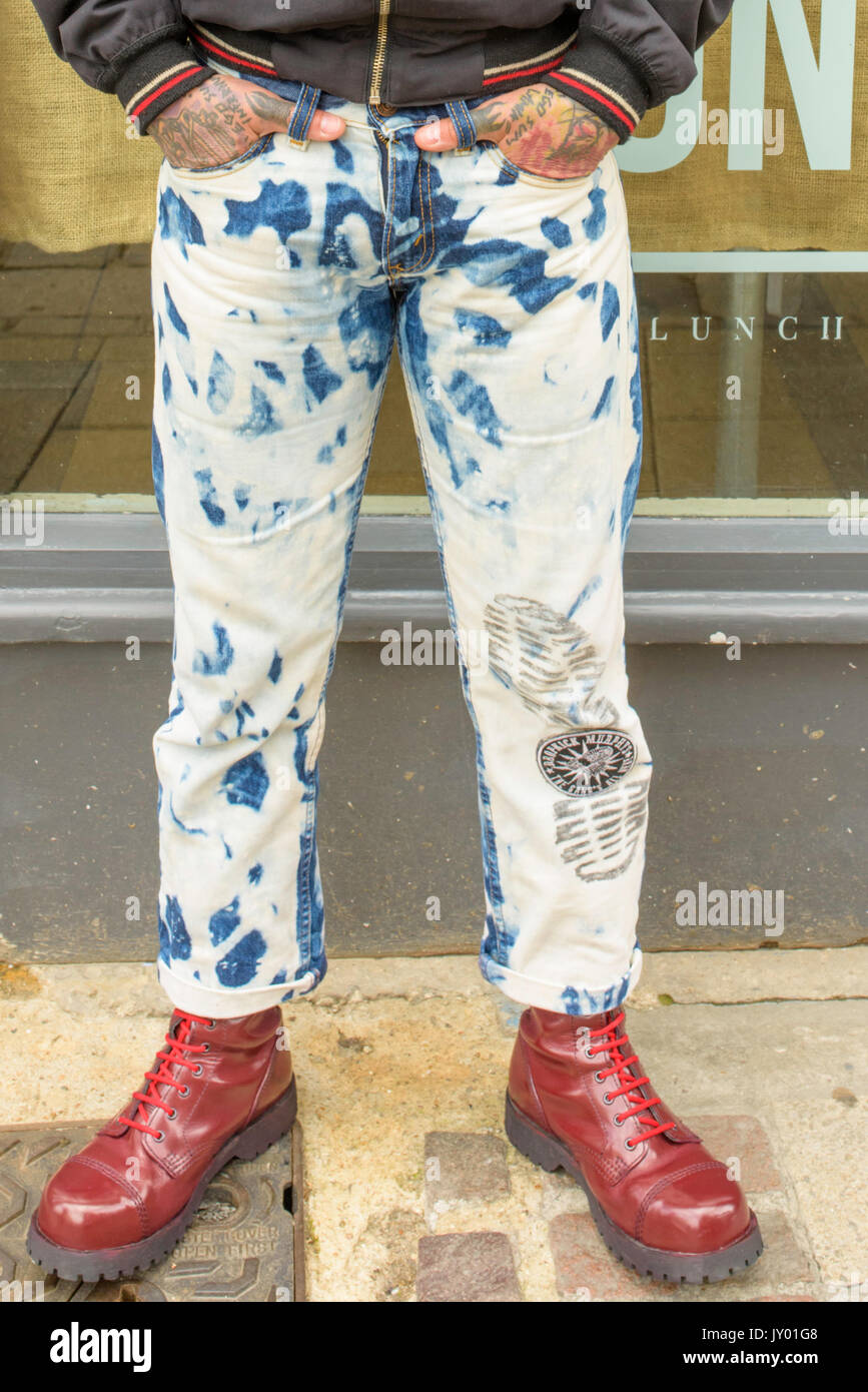 Male punk wearing tight, stonewashed jeans , with tattooed hands in his pockets and bright red Doc Martens boots on his feet. Stock Photo