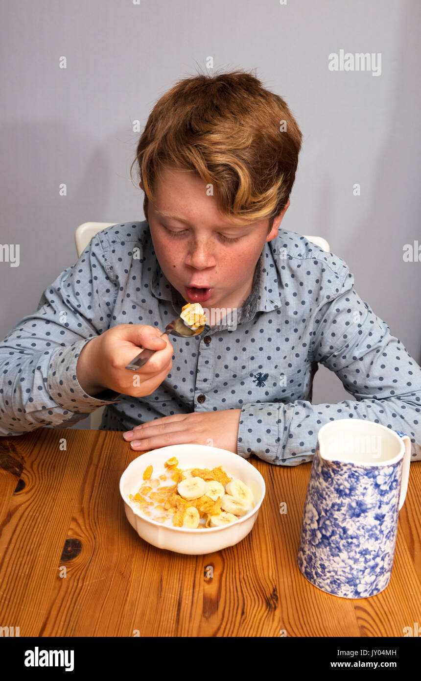 Boy eating cornflakes with sliced banana for breakfast hires stock