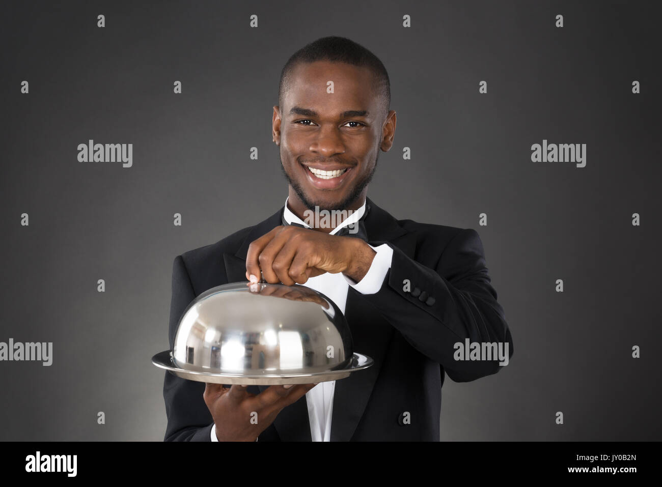 Portrait Of Happy Waiter Serving Meal In Cloche Stock Photo