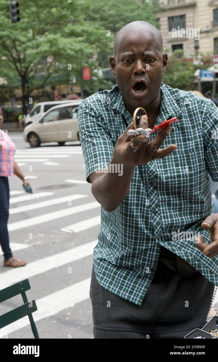 An expressive man selling fidget spinners demonstrates spinning several of them at one. In the Herald Square section of Manhattan, New York City. Stock Photo