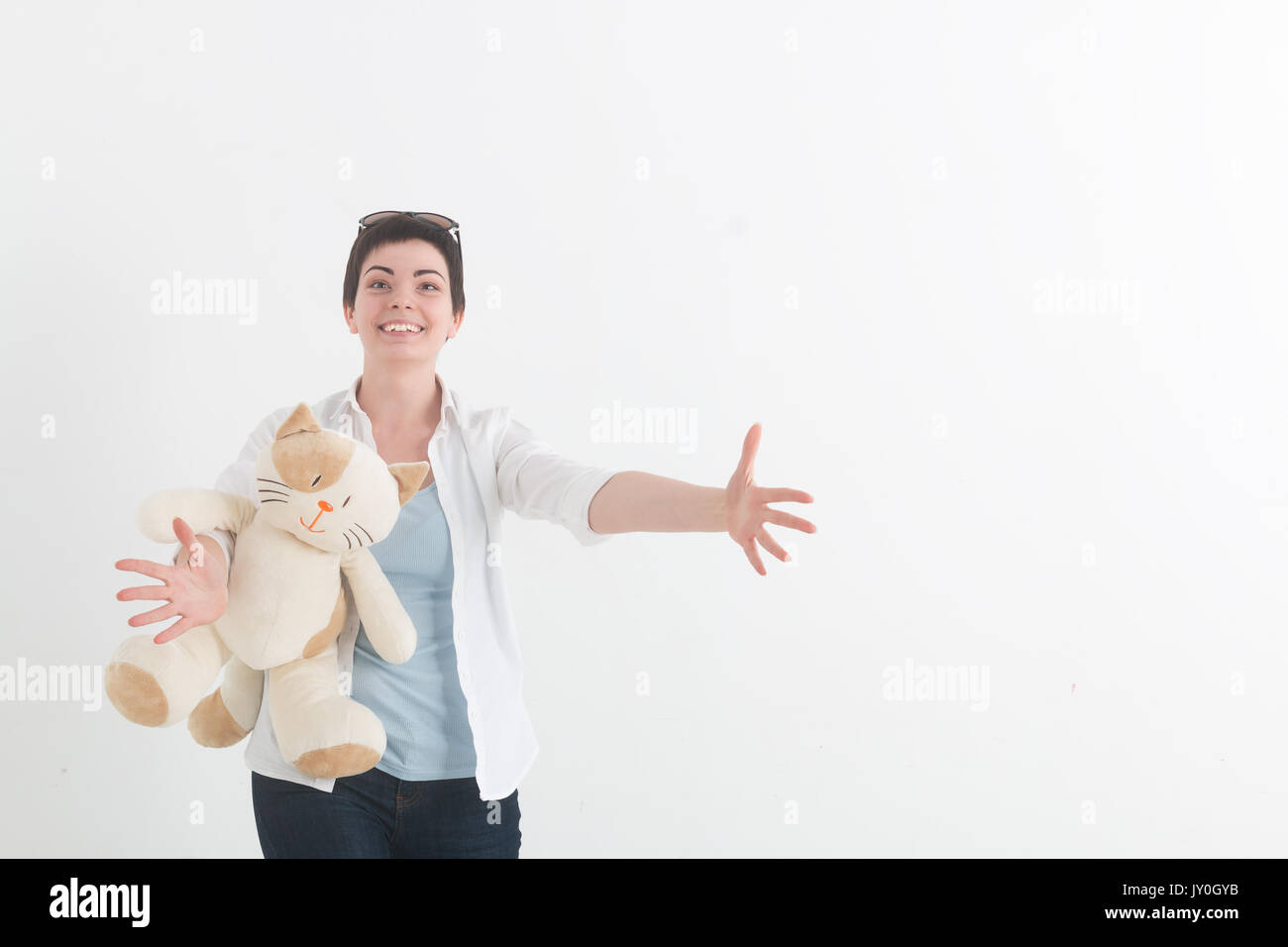 Young woman in a white blouse with cat is preparing to hug someone, spreading her hands wide apart and greeting smiling. Stock Photo