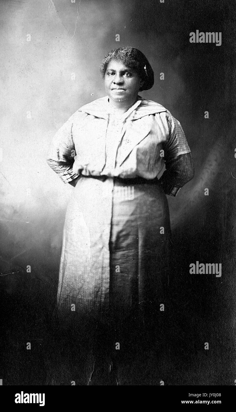 Portrait of an African American woman standing with her hands behind her back, she is wearing a light blouse which is tucked into a long light colored skirt, 1915. Stock Photo