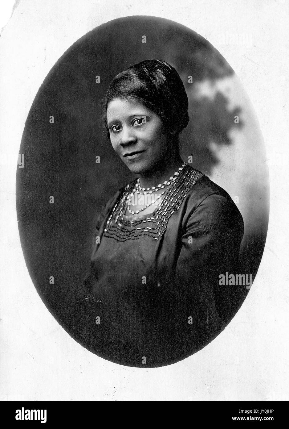 Oval half length portrait of an African American woman, she is wearing a dark shirt and light colored necklaces, 1915. Stock Photo