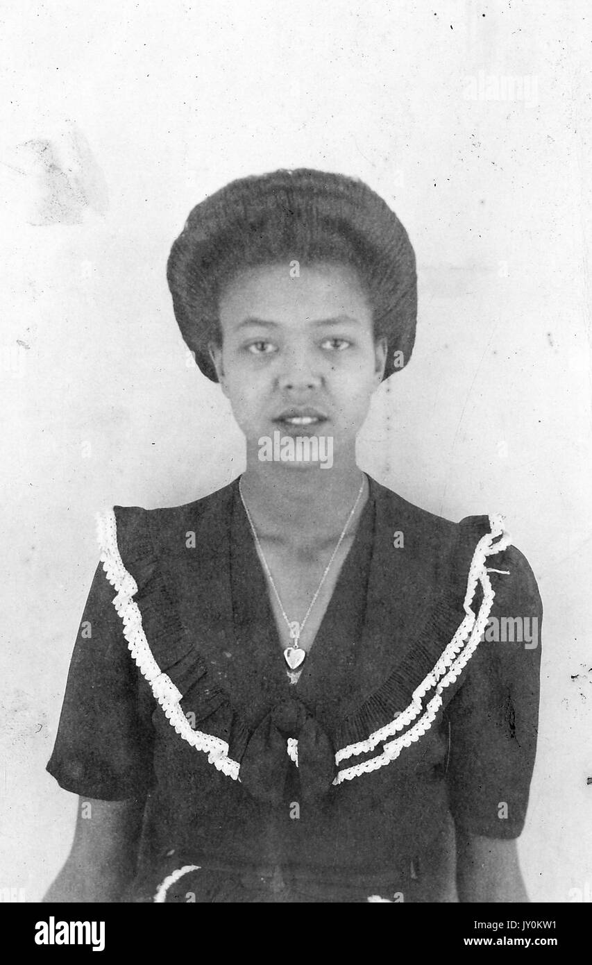 Headshot of mature African American woman, wearing dark dress with light lace detail and heart-shaped necklace, neutral expression, 1925. Stock Photo